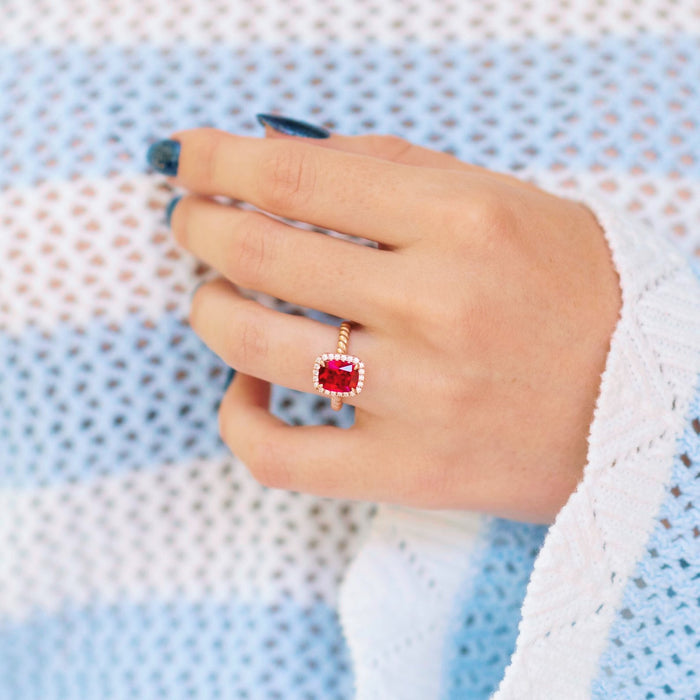 Ruby Engagement Ring Cushion Cut Ruby Halo Ring on hand over textured blue and white background