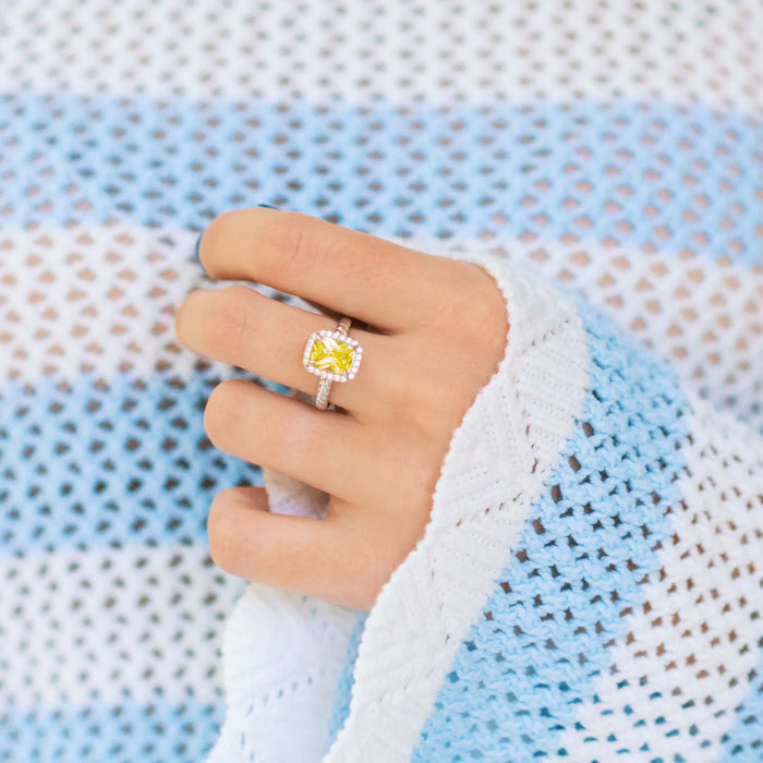 Hand wearing a ring with a yellow gemstone against a textured light blue and white background
