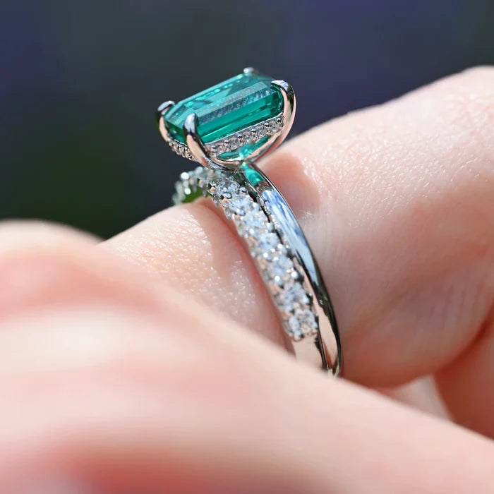 Emerald Engagement Ring in 14K White Gold (Hidden Halo) by Aquamarise Gold, showcasing a lab-grown emerald-cut emerald with diamond accents on a polished white gold band worn on a finger.