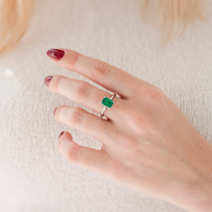 Emerald Engagement Ring in 14K White Gold (Hidden Halo) by Aquamarise Gold, featuring a vibrant emerald-cut lab-grown emerald on a sleek white gold band worn on a hand.