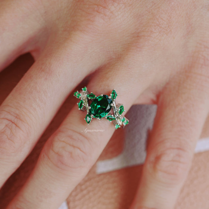 Oval Cut Lab-Grown Emerald Leaf Engagement Ring in 14K White Gold by Aquamarise Gold, featuring a vibrant oval emerald with intricate leaf-inspired design and sparkling accents on hand.