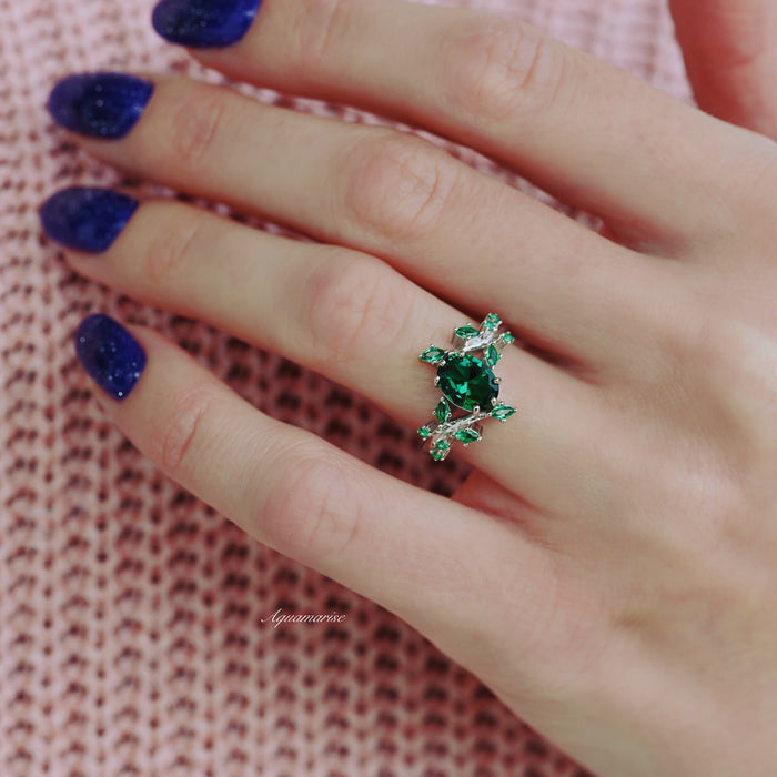 Oval Cut Lab-Grown Emerald Leaf Engagement Ring in 14K White Gold by Aquamarise Gold, showcasing a vivid green oval emerald with leaf-inspired design on hand with purple glitter nails.