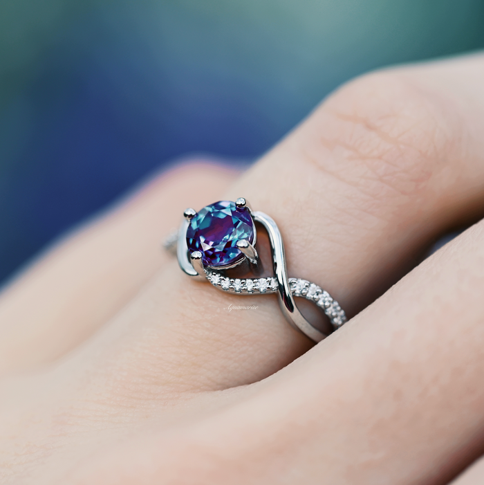 Entwined Teal & Purple Alexandrite Ring- Sterling Silver by Aquamarise, featuring a twisting band with pavé diamonds and a color-changing teal and purple alexandrite center stone on a finger.