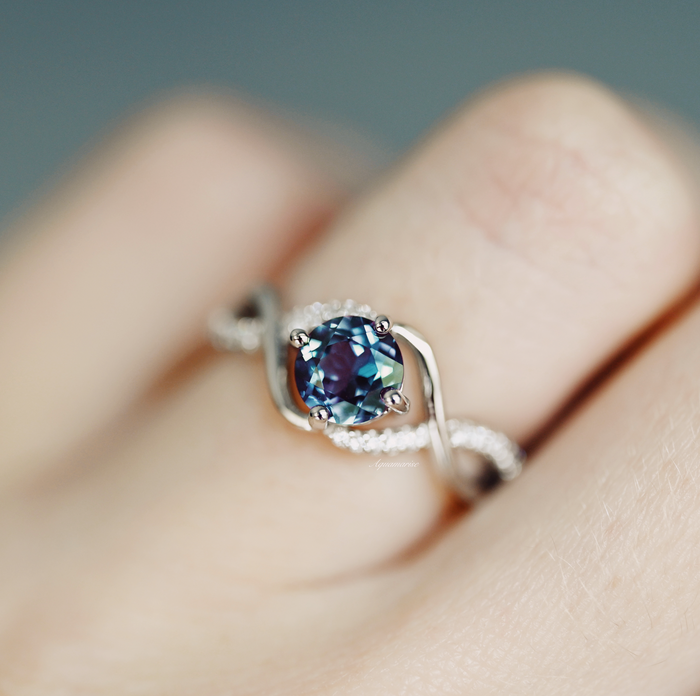 Entwined Teal & Purple Alexandrite Ring- Sterling Silver by Aquamarise, featuring a delicate twisting band with pavé accents and a color-changing teal and purple alexandrite center stone on a finger.