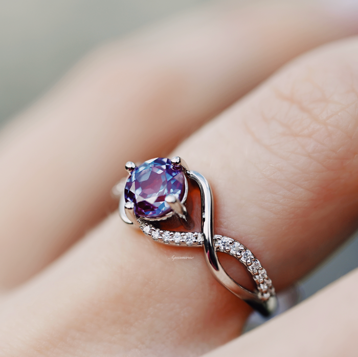 Entwined Teal & Purple Alexandrite Ring- Sterling Silver by Aquamarise, featuring a twisting band with pavé accents and a color-changing teal and purple alexandrite center stone on a finger.