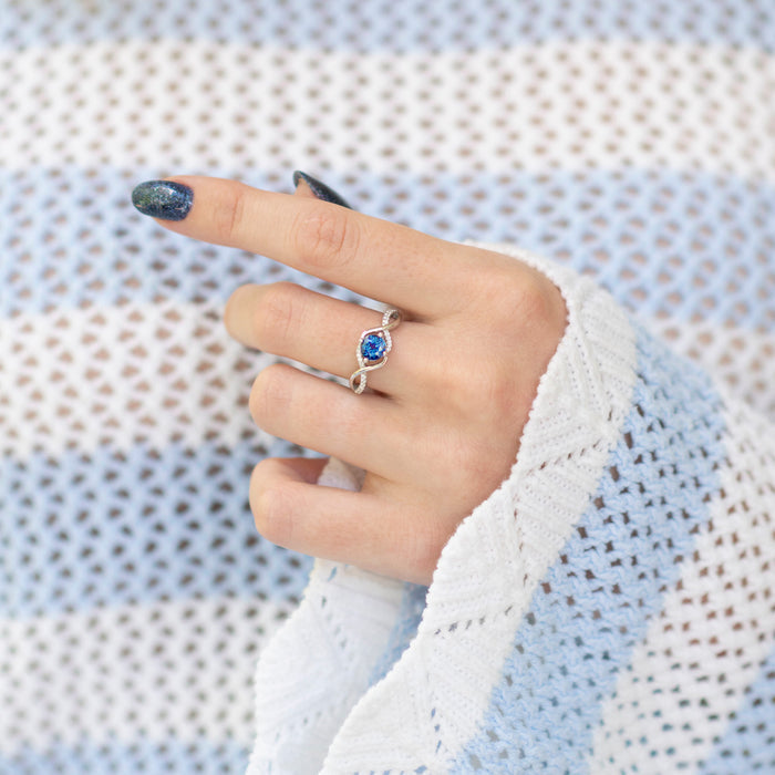Entwined Teal & Purple Alexandrite Ring- Sterling Silver by Aquamarise, featuring a twisting band and a color-shifting teal and purple alexandrite stone on a hand with glittery nail polish.