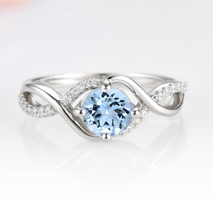 Entwined Aquamarine Ring- Sterling Silver by Aquamarise, featuring a delicate twisting band accented with pavé stones and a central round aquamarine gemstone in soft blue.