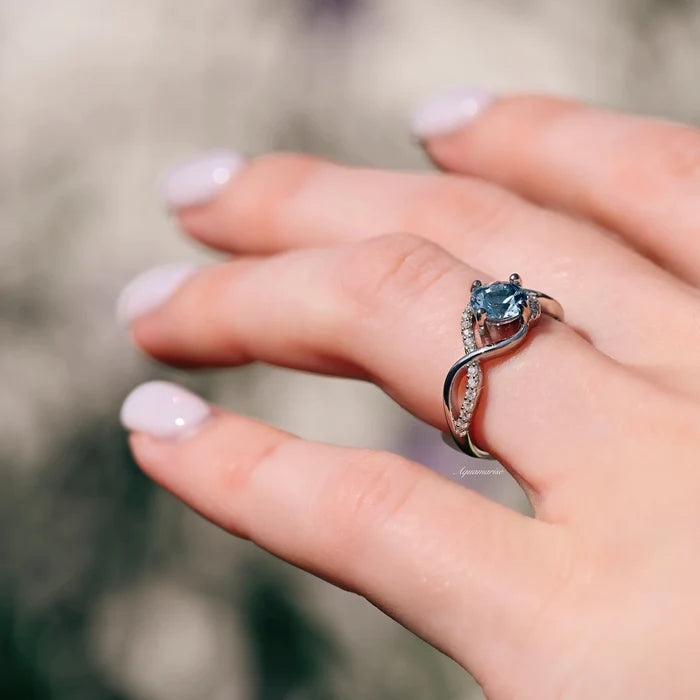 Entwined Aquamarine Ring- Sterling Silver by Aquamarise, showcasing a twisted band with pavé accents and a vibrant blue aquamarine stone on a hand with natural light.