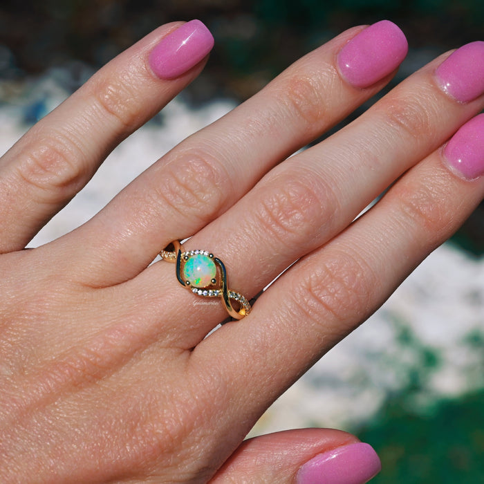 Entwined Natural Australian Opal Engagement Ring in 14K Solid Yellow Gold by Aquamarise Gold, featuring an opal centerpiece with intertwined gold and diamond accents on a hand.