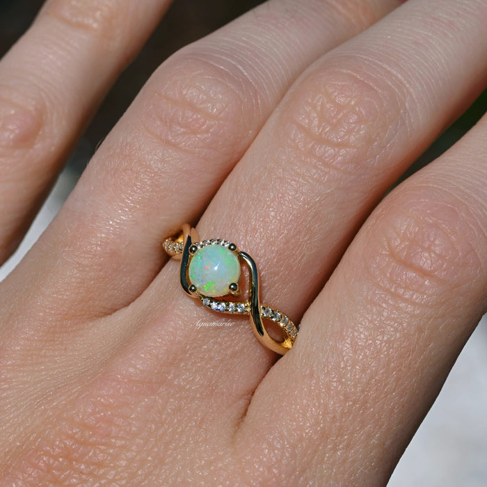 Entwined Natural Australian Opal Engagement Ring in 14K Solid Yellow Gold by Aquamarise Gold, featuring an opal center set in a twisted gold band with diamond accents on a hand.
