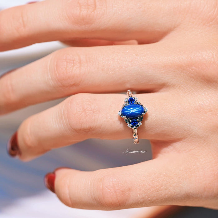 Esme Natural Star Sapphire Engagement Ring in Sterling Silver by Aquamarise featuring a radiant star sapphire surrounded by intricate silver and blue gemstone details on a hand.