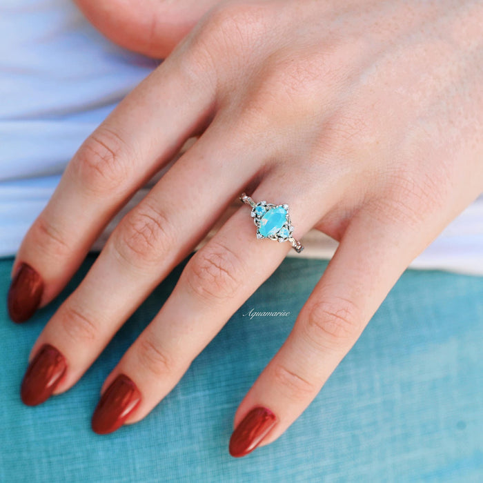 Esme Opalescent Blue Sapphire Mermaid Ring in 925 Sterling Silver showcasing a light blue sapphire centerpiece with delicate silver detailing, styled on a hand with deep red nails.