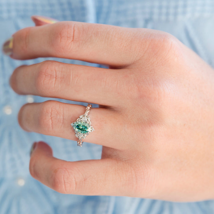 Esme Oval Cut Teal Moissanite Engagement Ring in 14K White Gold worn on hand, featuring a teal center stone surrounded by sparkling accents by Aquamarise Gold.