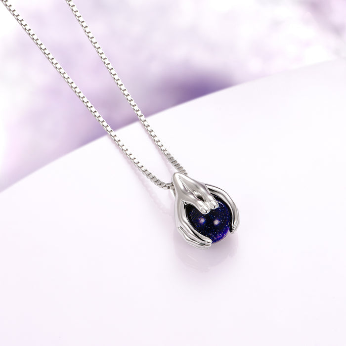 Ethereal Hold Starry Night Pendant Necklace in Sterling Silver by Aquamarise, featuring sculpted sterling silver hands cradling a luminous deep blue starry orb, part of Night Court Jewelry and Meaningful Jewelry Gifts collections.