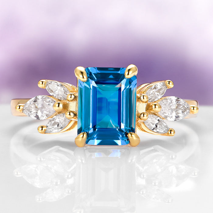 Eva London Blue Topaz Engagement Ring in 14K Solid Yellow Gold by Aquamarise Gold featuring an emerald-cut blue topaz with marquise-cut white stone accents in a vintage-inspired design.