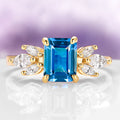 Eva London Blue Topaz Engagement Ring in 14K Solid Yellow Gold by Aquamarise Gold featuring an emerald-cut blue topaz with marquise-cut white stone accents in a vintage-inspired design.