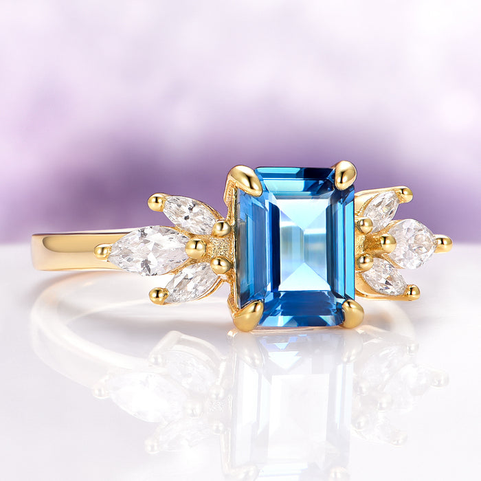 Eva London Blue Topaz Engagement Ring in 14K Solid Yellow Gold by Aquamarise Gold featuring an emerald-cut blue topaz with marquise and pear-shaped white stone accents.