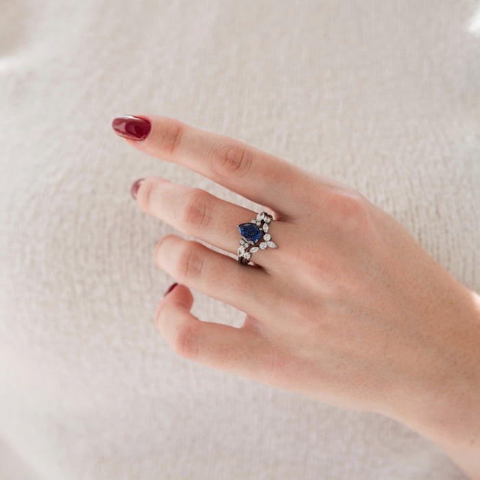 Evelyn Starry Night Ring Set in Black Ruthenium by Aquamarise featuring a pear-shaped blue gemstone with sparkling simulated diamonds on black rhodium sterling silver bands.