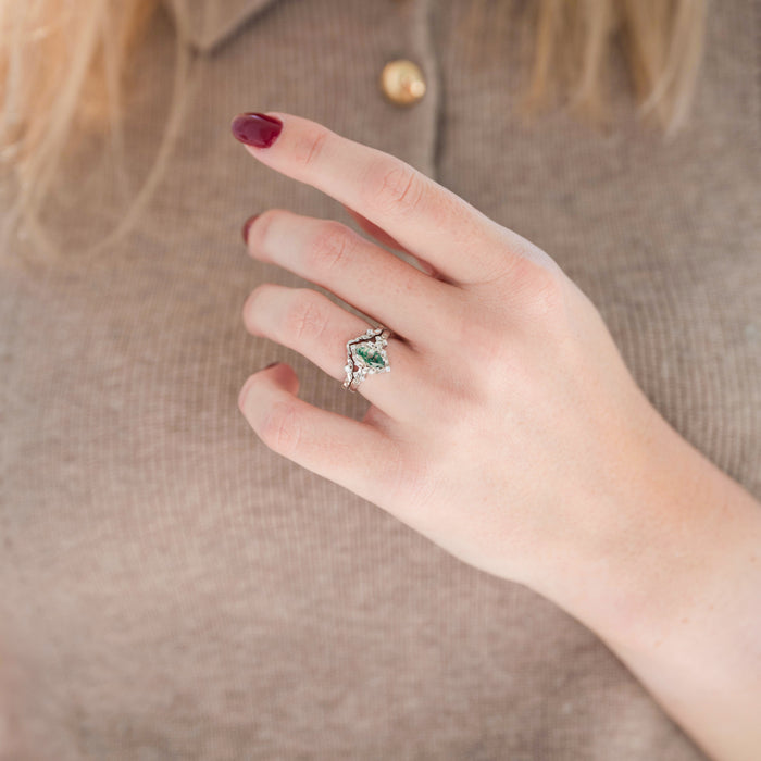 Sterling silver wedding band with leaf motif and marquise moss agate engagement ring displayed in hand against warm brown backdrop