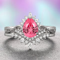 A fantasy cut pink sapphire engagement ring set in 14K white gold, with Moissanite accent stones on the band, displayed against a gradient purple and pink background.