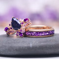 Feyra Starry Night & Amethyst Couples Ring Set featuring a pear-shaped deep blue starry night gemstone with intricate rose gold floral accents and a matching band inlaid with crushed amethyst stones, crafted by Aquamarise.