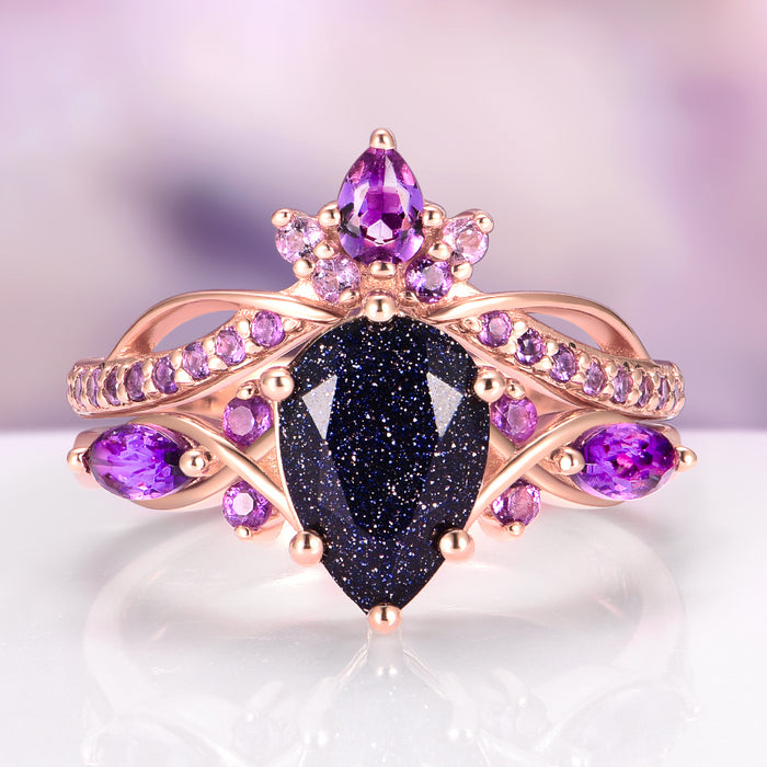 Feyra Starry Night & Amethyst Couples Ring Set featuring a pear-shaped dark blue sandstone center stone surrounded by vibrant amethyst gemstones set in a delicate rose gold band, crafted by Aquamarise for Matching Couples' Rings and February Birthstone collections.