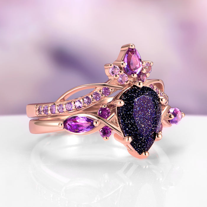 Feyra Starry Night & Amethyst Couples Ring Set by Aquamarise featuring a pear-shaped deep blue sandstone center stone accented with various purple amethyst gemstones on an intricate rose gold band, part of Matching Couples' Rings and Starry Night™ Rings collections.