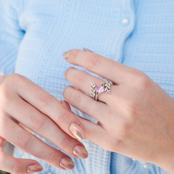 Close-up of a hand wearing a pink gemstone ring with a silver band against a light blue shirt background.
