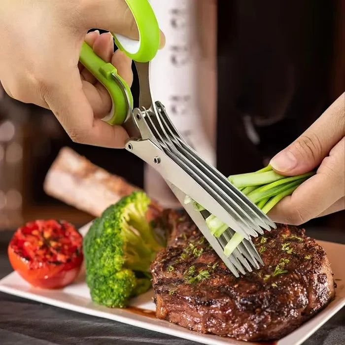 Person using five blade herb scissors to chop green onions beside a steak and vegetables.