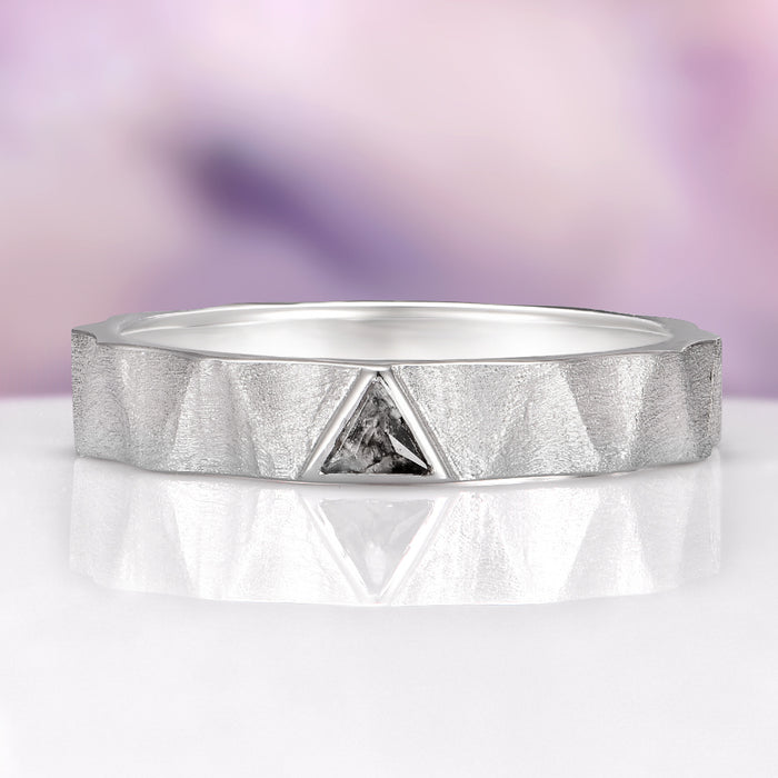 Silver ring with a diamond on a reflective surface and blurred purple background