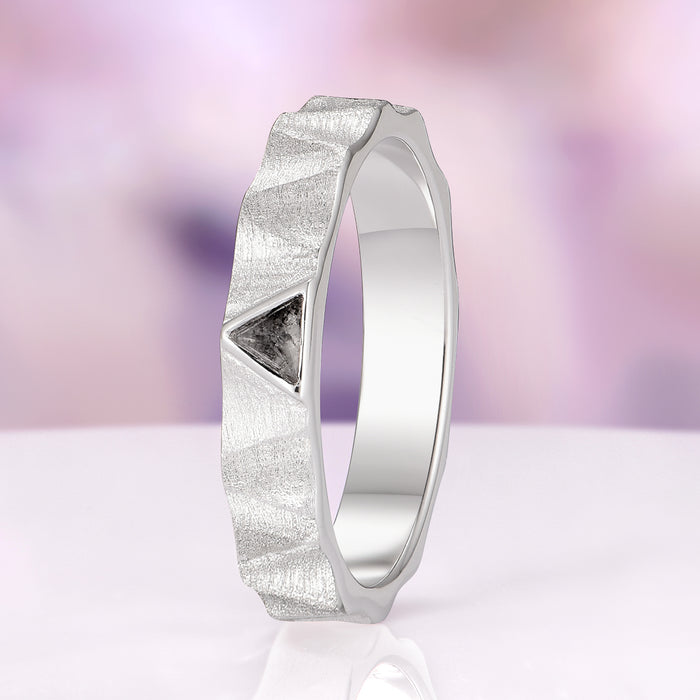 Silver ring with textured surface and triangular design element on a blurred purple background