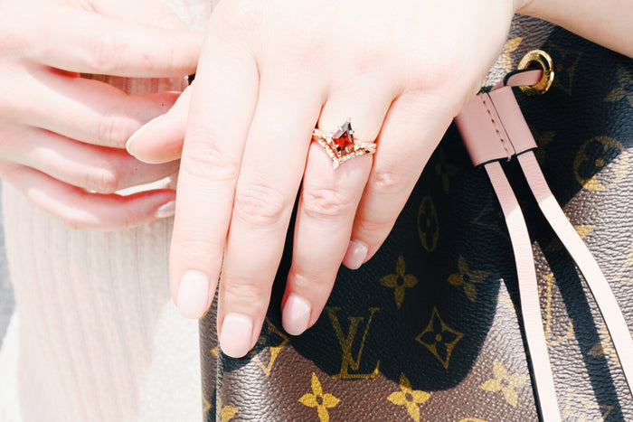 Garnet & Red Fire Opal Whiskey Barrel Couples Ring Set by Aquamarise showcasing a kite-cut garnet with diamond accents on a hand against a luxury handbag, perfect for matching couple rings.