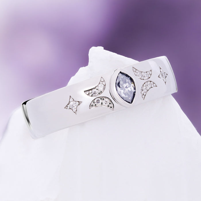 Gray moissanite celestial wedding band resting on white stone, crescent moons and four-point stars around the marquise center