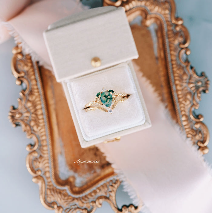 Green Moss Agate Leaf Engagement Ring Set in 14K Solid Yellow Gold by Aquamarise Gold, with a pear-shaped green moss agate gemstone surrounded by delicate feather-inspired gold detailing, displayed in a white ring box on an ornate gold tray.
