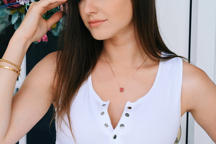 Woman wearing a white sleeveless top with a necklace featuring a red pendant.