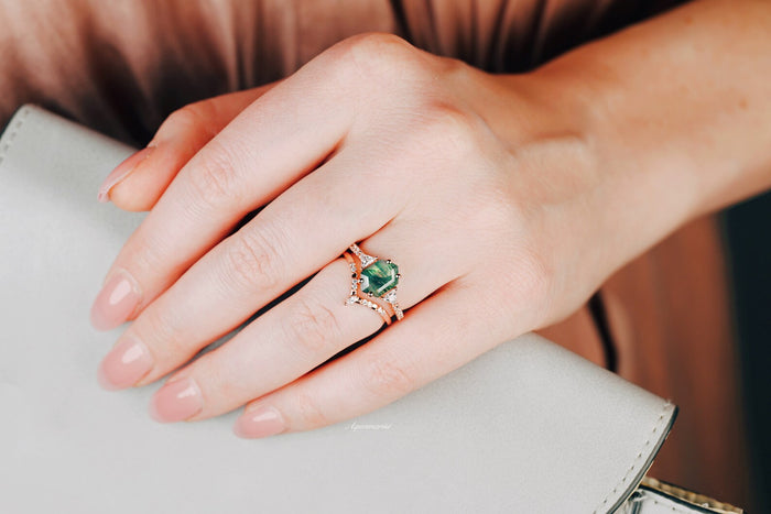 Hexagon Cut Green Moss Agate Engagement Ring Set in 14K Solid Rose Gold by Aquamarise Gold, featuring a unique green moss agate stone and delicate rose gold bands on a hand holding a light gray purse.