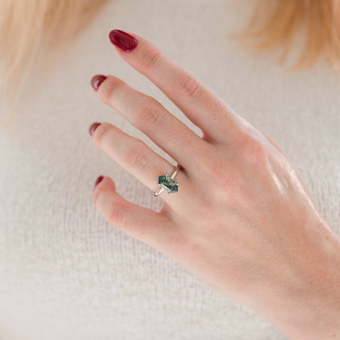 Hand wearing a silver ring with a green gemstone on a light background