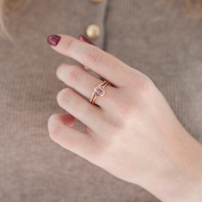 Rose gold hexagon-shaped pink morganite engagement ring with diamond accent stones and adjustable wedding band displayed in hand against warm brown backdrop