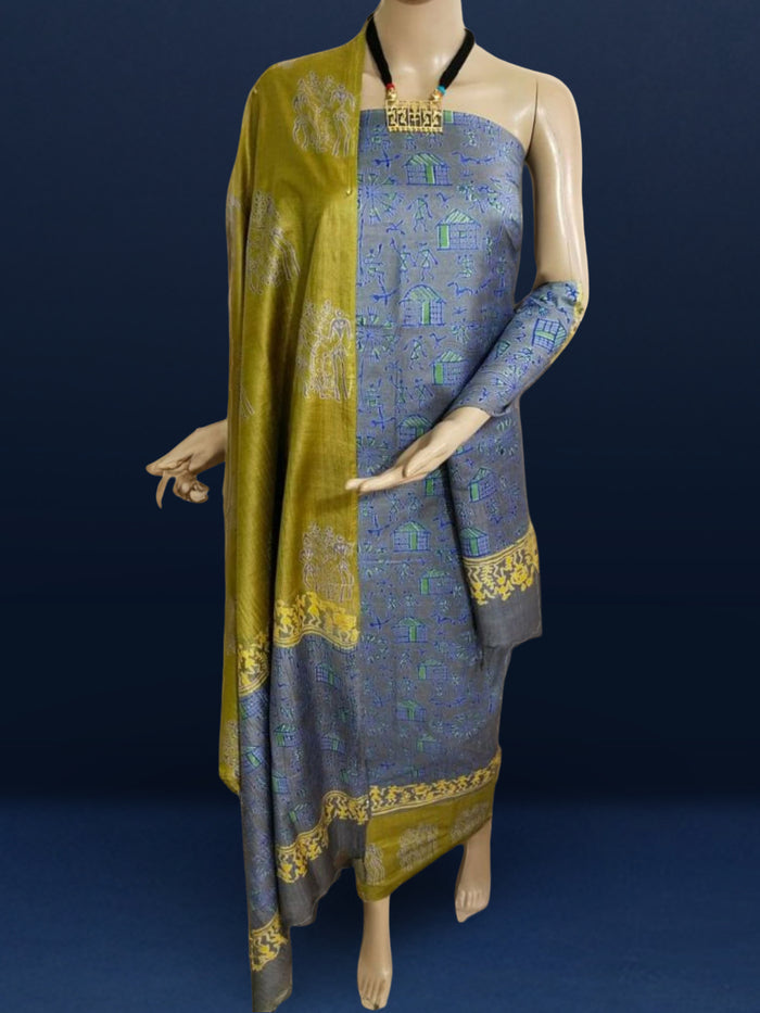 Unstitched Katan silk suit set with deep indigo panels block printed in folk figure silhouettes and geometric shapes, a plain olive green piece, and mustard yellow figurative border bands at the edges and dupatta ends.