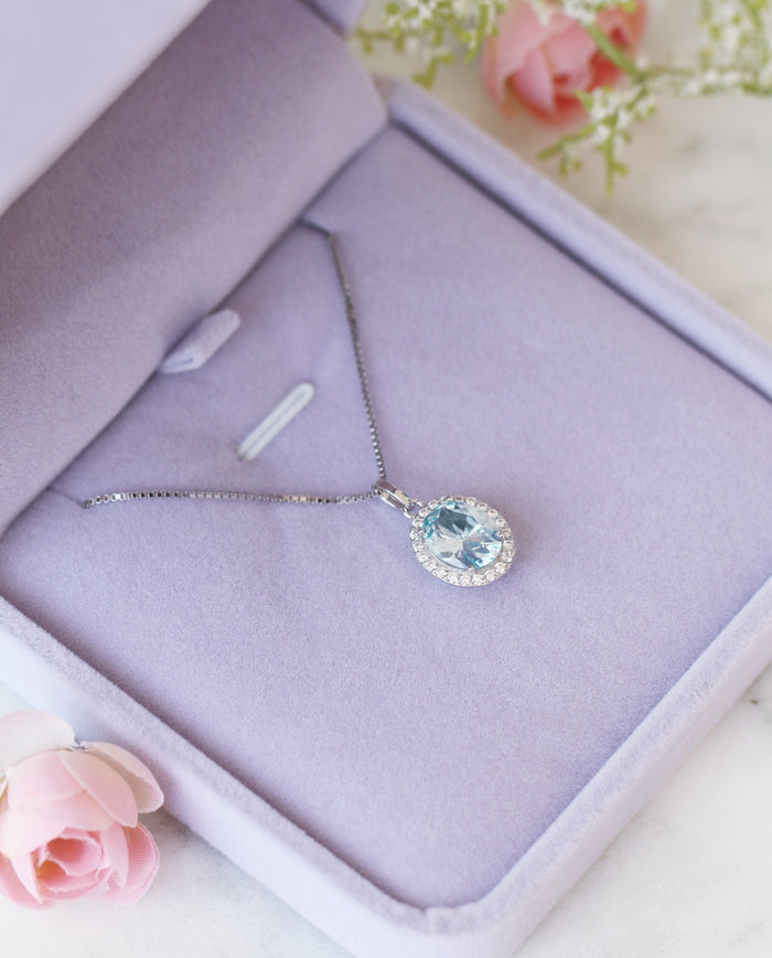 Iris Halo Oval Aquamarine Necklace in Sterling Silver featuring a 2.3 ct simulated aquamarine surrounded by sparkling simulated diamonds in a soft purple jewelry box by Aquamarise.