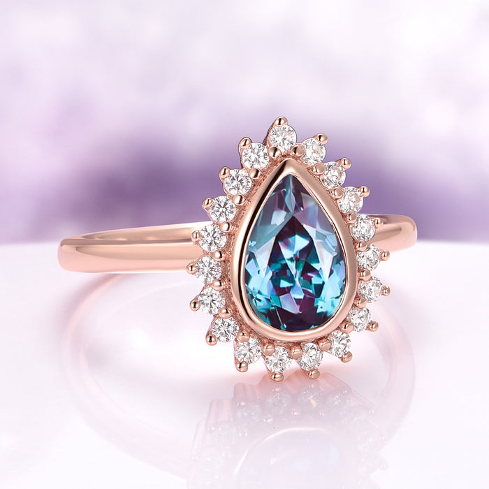 Rose gold ring with a teardrop-shaped blue gemstone and diamond accents on a soft purple background.