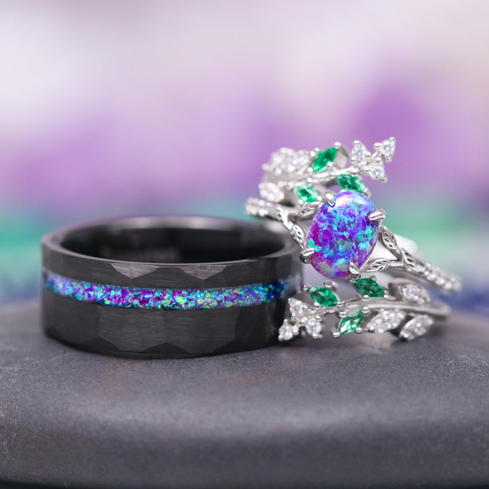 Lavender Fire Opal & Emerald Leaf Couples Ring Set featuring a hammered black band with a vibrant purple and blue opal inlay alongside an intricately designed silver band with a central lavender fire opal surrounded by green emerald leaves, crafted by Aquamarise.