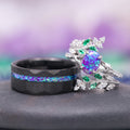 Lavender Fire Opal & Emerald Leaf Couples Ring Set featuring a hammered black band with a vibrant purple and blue opal inlay alongside an intricately designed silver band with a central lavender fire opal surrounded by green emerald leaves, crafted by Aquamarise.