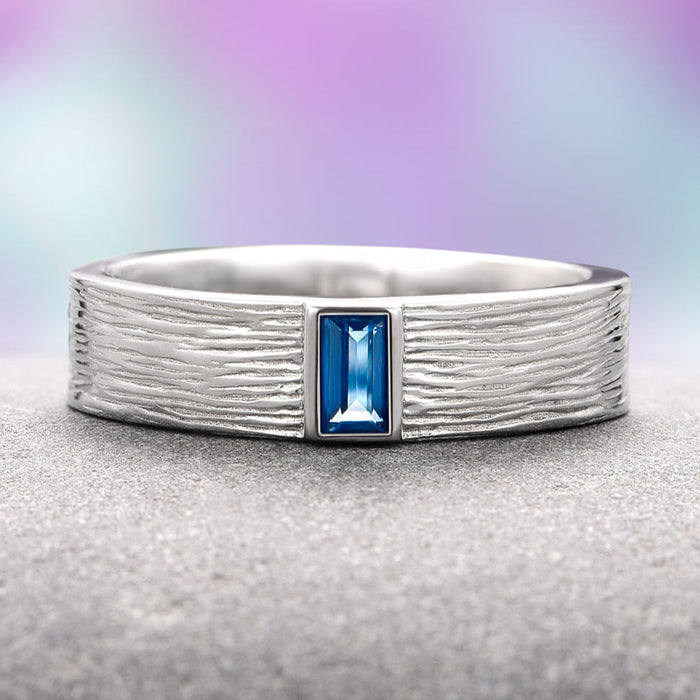 Rustic London Blue Topaz Wedding Band- 14K White Gold featuring a textured white gold band inspired by natural elements with a rectangular emerald-cut London Blue Topaz center stone, crafted by Aquamarise Gold, part of Solid Gold Engagement Rings, Men’s Wedding Bands, November Birthstone, and Nature Inspired Jewelry collections.