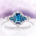 Emerald Cut London Blue Topaz Leaf Engagement Ring in 14K White Gold by Aquamarise Gold featuring a deep blue emerald-cut stone with diamond accents in a nature-inspired Art Deco design.