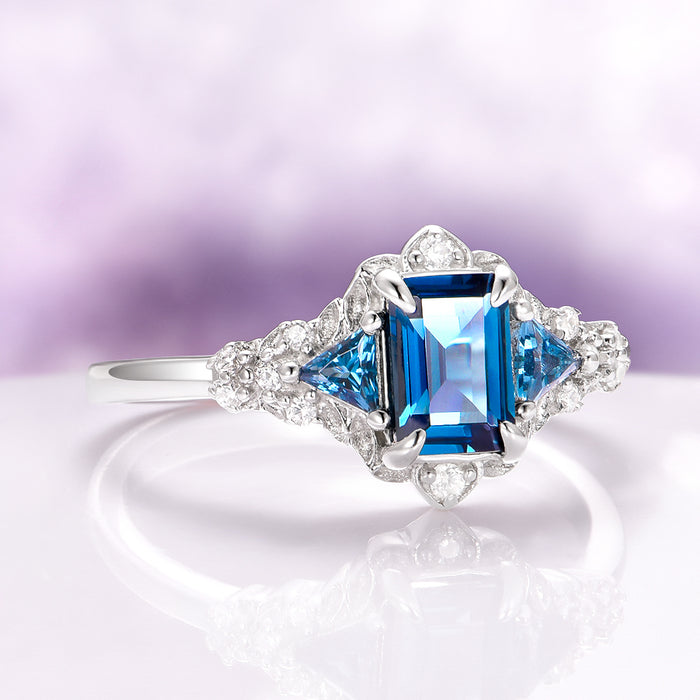Emerald Cut London Blue Topaz Leaf Engagement Ring in 14K White Gold by Aquamarise Gold featuring a deep blue emerald-cut topaz with triangular accents in a nature-inspired design.