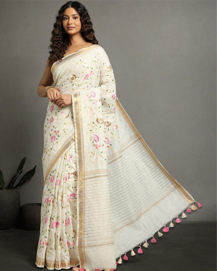 A model wearing an off-white silk linen embroidered saree with floral patterns and a beige border.