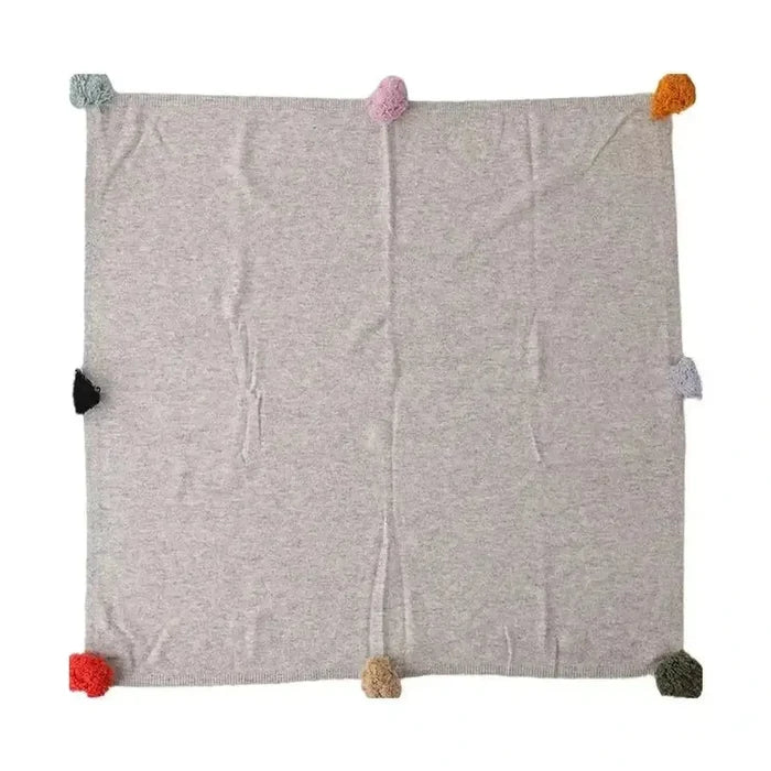 Luxury cashmere throw blanket with colorful pom-poms, perfect for cozy evenings.