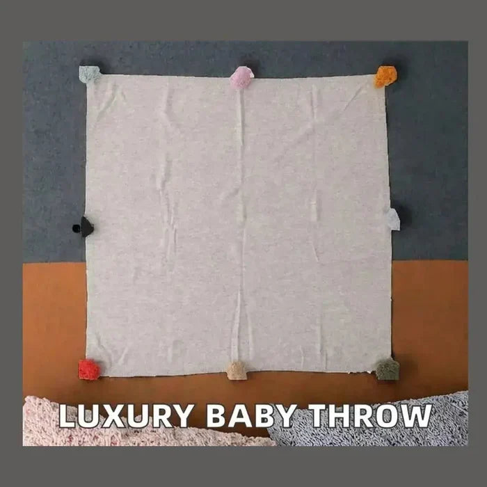 Luxury cashmere throw blanket in soft gray with colorful pom-poms, perfect for cozy evenings.