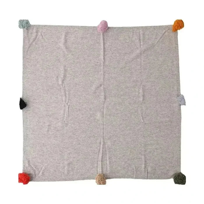 Luxury cashmere throw blanket with colorful pom-poms for a cozy feel.